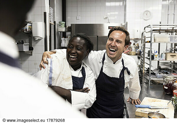 Happy chef with arm around female colleague in commercial kitchen