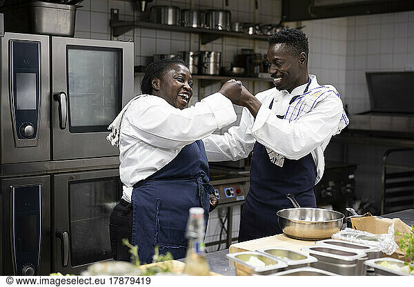 Happy chefs fist bumping while working in restaurant