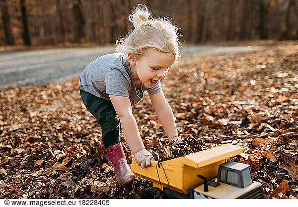 Happy child playing in fall leaves with toy truck