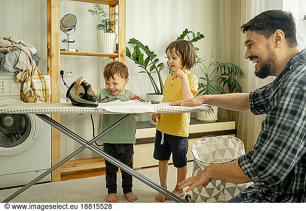 Happy children helping father ironing clothes at home