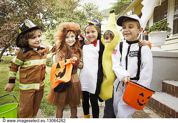 Happy children in Halloween costumes standing in yard during trick or treating