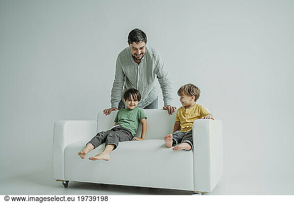 Happy children sitting on sofa with father standing against white background