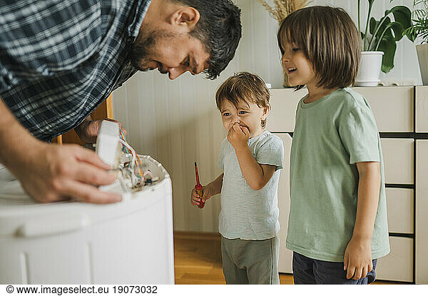Happy children watching father repairing washing machine at home