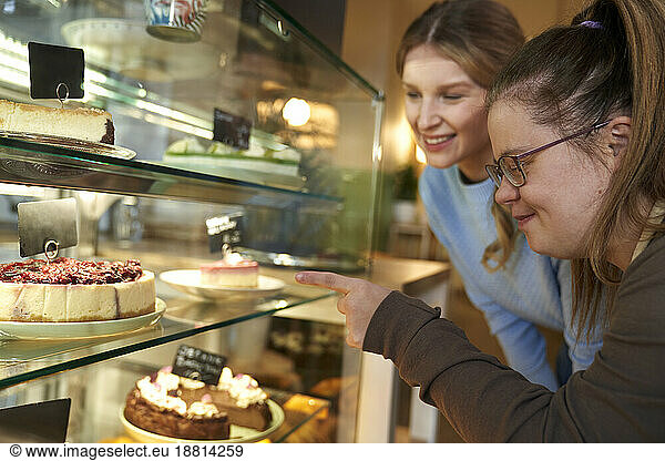 Happy coffee shop owner with down syndrome advising customer to choose cake in cafe