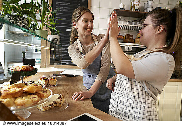 Happy coffee shop owner with down syndrome giving high-five in cafe