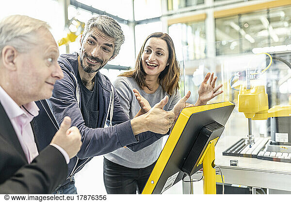 Happy colleagues giving thumbs up in robotic factory