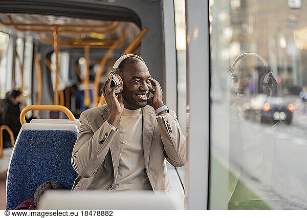 Happy commuter wearing wireless headphones and looking out of window in tram