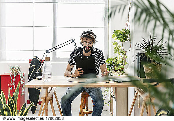 Happy content creator with clipboard recording podcast through microphone at home