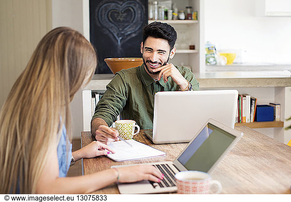 Happy couple discussing while using laptops at home