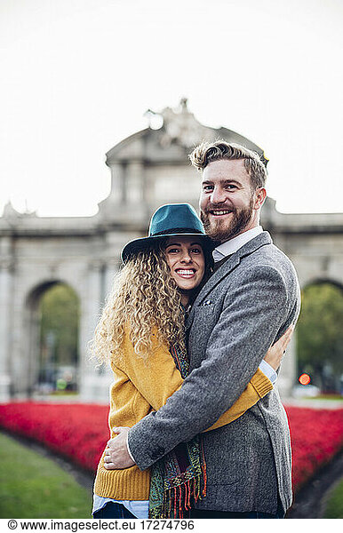 Happy couple embracing each other while standing against gate in city