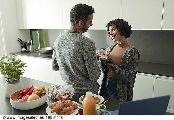 Happy couple enjoying breakfast and coffee in morning kitchen