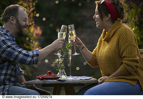 Happy couple enjoying champagne and red currants at patio table