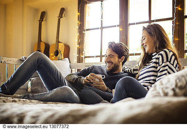 Happy couple having coffee while resting on alcove window seat at home