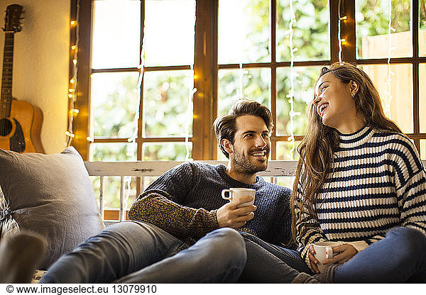 Happy couple having coffee while sitting on alcove window seat at home