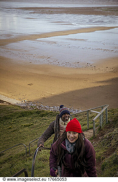 Happy couple hiking up steps over winter beach