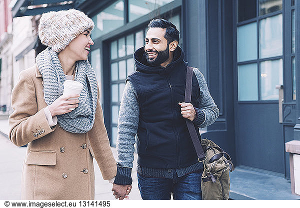 Happy couple holding hands while walking on footpath in city