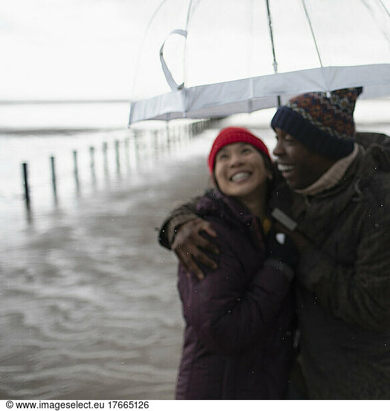 Happy couple in warm clothing under umbrella on wet winter beach