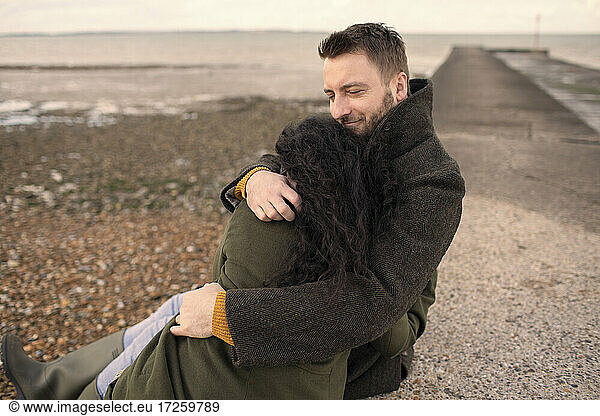 Happy couple in winter coats hugging on ocean jetty