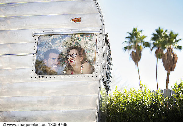 Happy couple looking through window while sitting in camper van