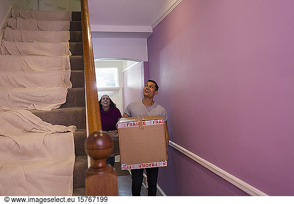Happy couple moving into new house  carrying cardboard boxes in corridor