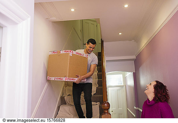 Happy couple moving out of house  carrying cardboard box down stairs