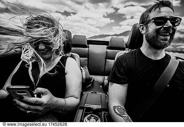 Happy couple on a road trip in a convertible car driving in mountains