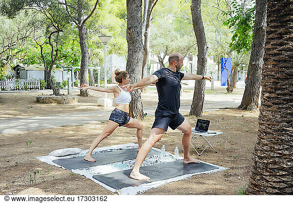 Happy couple practicing yoga in line in the forest. They practice sport in line outdoors. Healthy life style. Copy space.