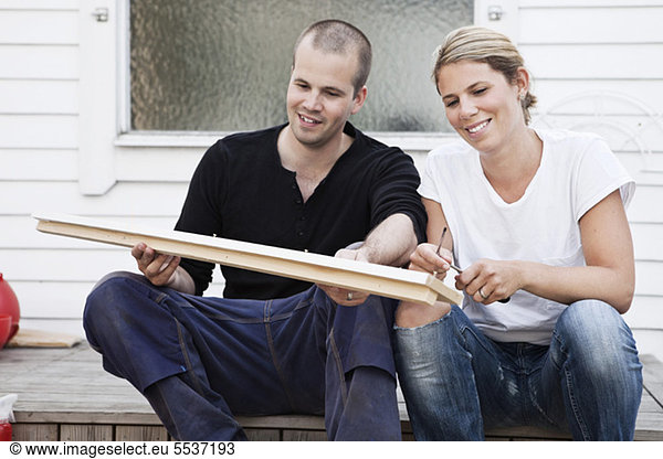 Happy couple sitting in front of house holding plank