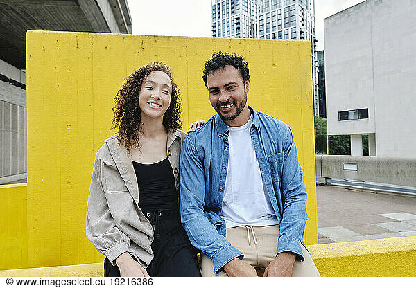 Happy couple sitting in front of yellow wall