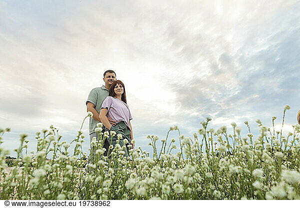 Happy couple standing in flower field under sky