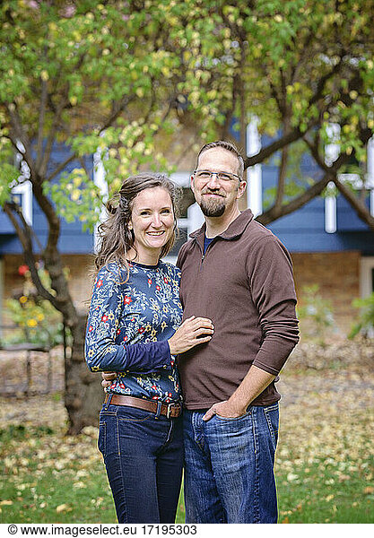 Happy couple standing in front of blue house and trees.