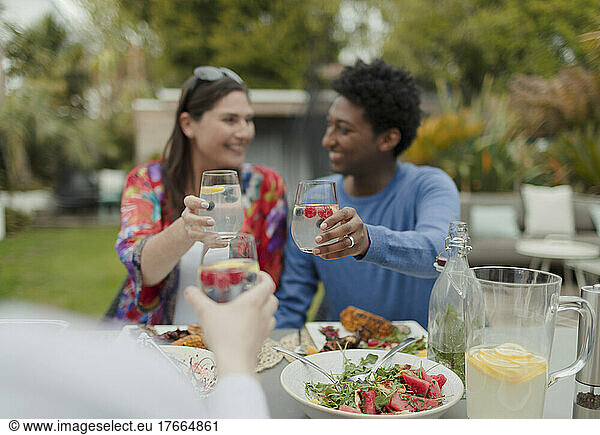 Happy couple toasting glasses with friend at patio table