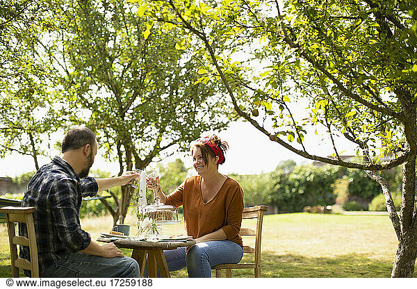Happy couple toasting water glasses at table in sunny summer garden