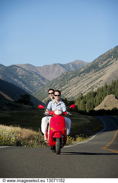 Happy couple traveling on motor scooter against mountains