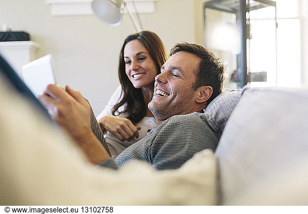 Happy couple using digital tablet while relaxing on sofa at home
