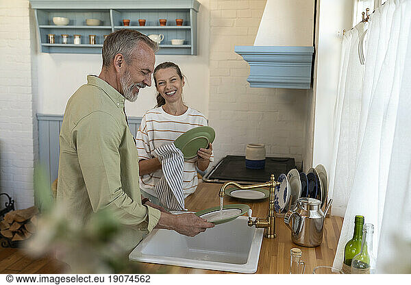 Happy couple washing dishes in kitchen at home
