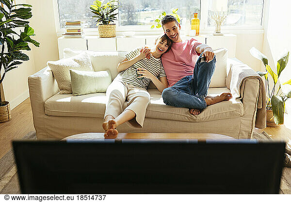 Happy couple watching TV sitting on sofa at home
