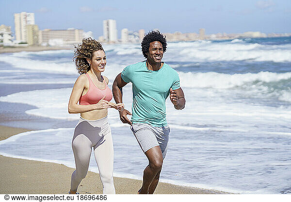 Happy couple wearing sportswear running at seashore