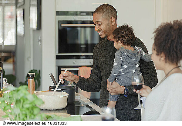Happy couple with baby daughter cooking dinner in kitchen