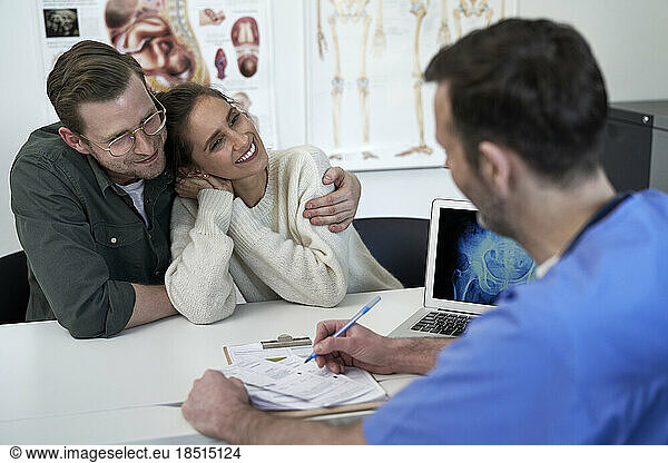 Happy couple with doctor discussing over prescription in clinic