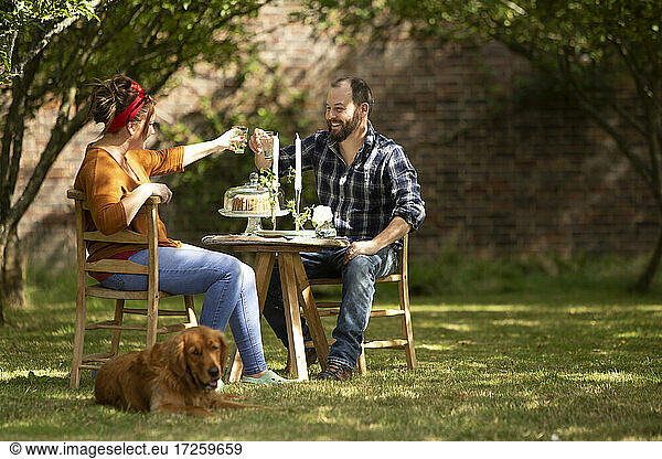 Happy couple with dog toasting glasses at table in summer garden