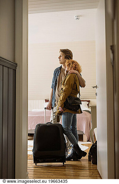 Happy couple with suitcase standing in hotel room
