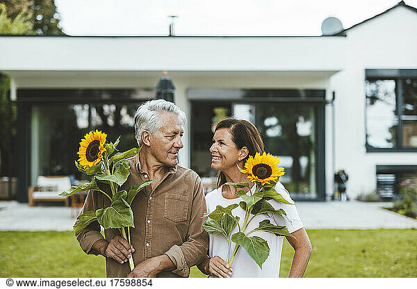 Happy couple with sunflowers looking at each other in garden