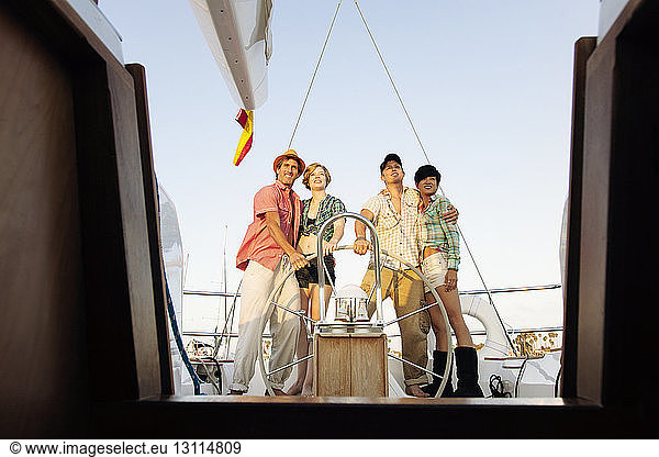 Happy couples standing by steering wheel on nautical vessel