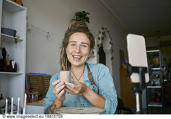 Happy craftswoman holding clay cup at workshop