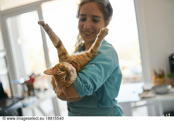Happy craftswoman playing with cat at workshop