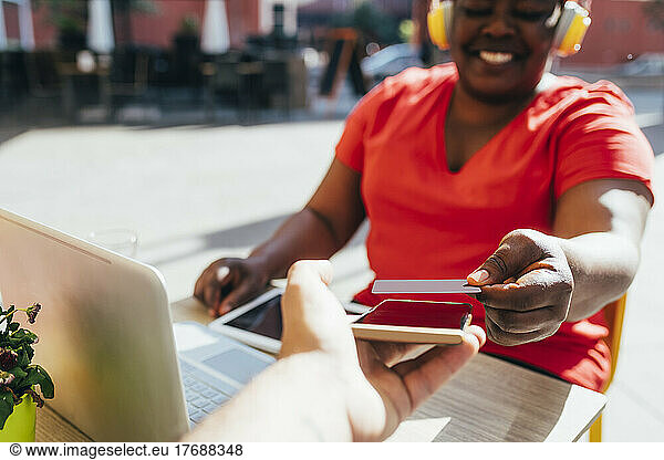 Happy customer making contactless payment through credit card at sidewalk cafe