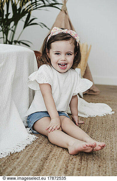 Happy cute girl sitting on carpet in living room