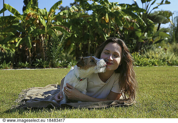 Happy cute puppy licking woman lying on grass