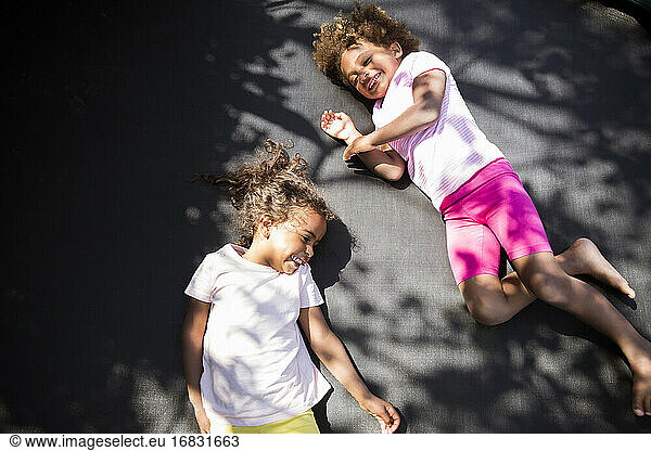 Happy cute sisters laying on sunny trampoline
